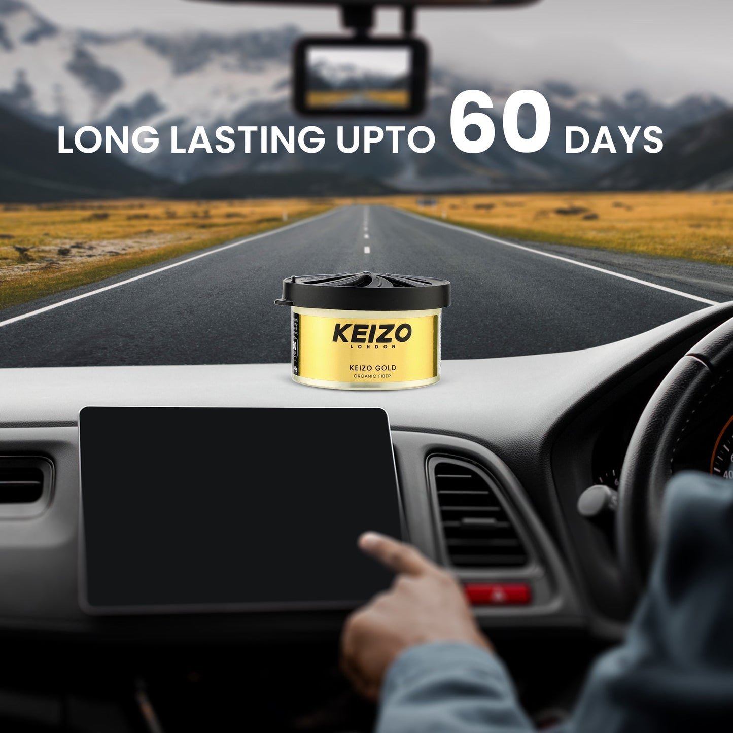 A hand on a car dashboard points to a can of Keizo London Gold 40g Car Perfume by Keizo placed above the dashboard, with text LONG LASTING UP TO 60 DAYS set against a scenic road and mountain background.
