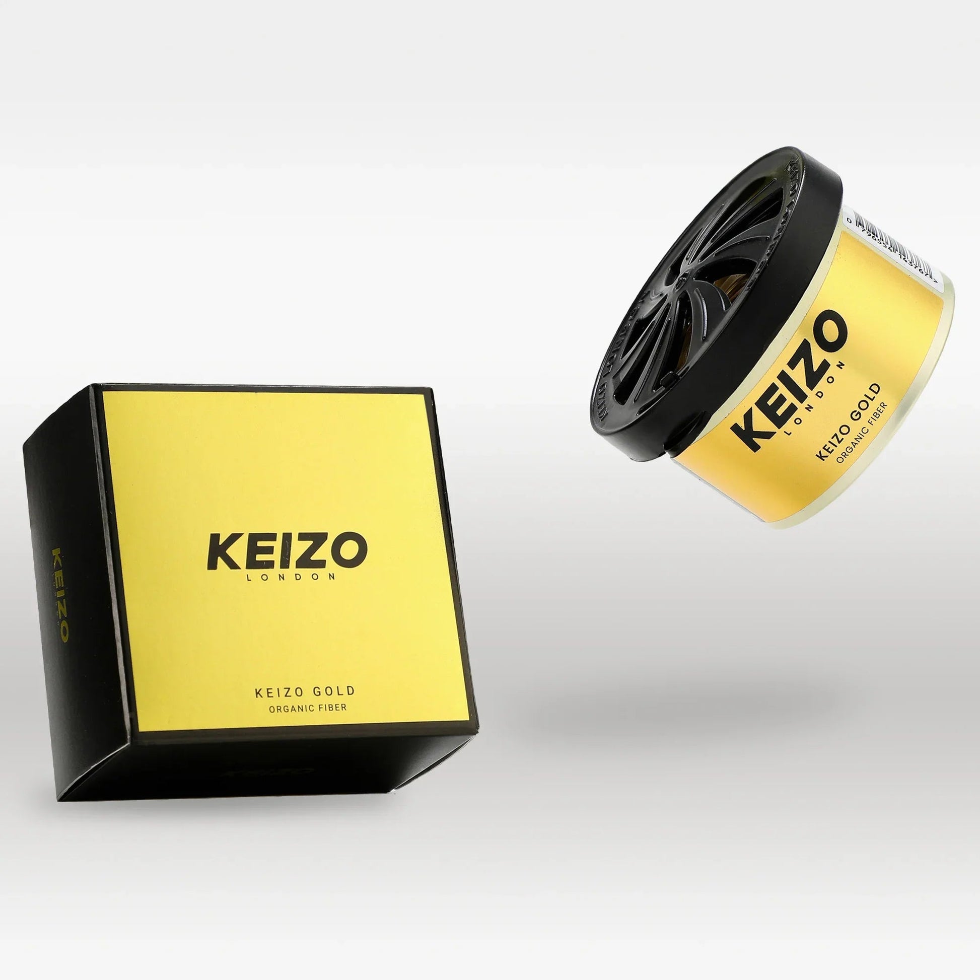 A yellow and black Keizo London Gold 40g Car Perfume box sits on a white surface, with a matching round perfume container nearby, both showcasing the Keizo brands luxury and golden organic fiber scent.